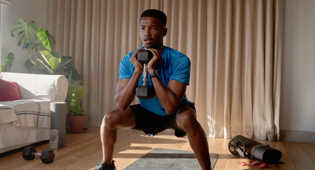 male-exercising-from-home-concentrating-while-squatting-with-a-dumbbell