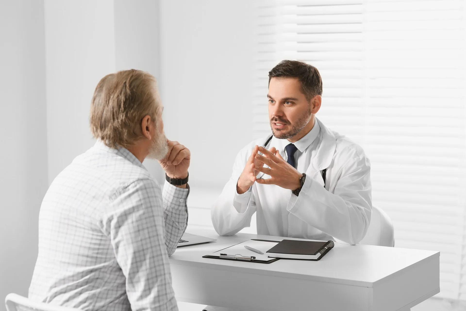 Doctor,Consulting,Senior,Patient,At,White,Table,In,Clinic